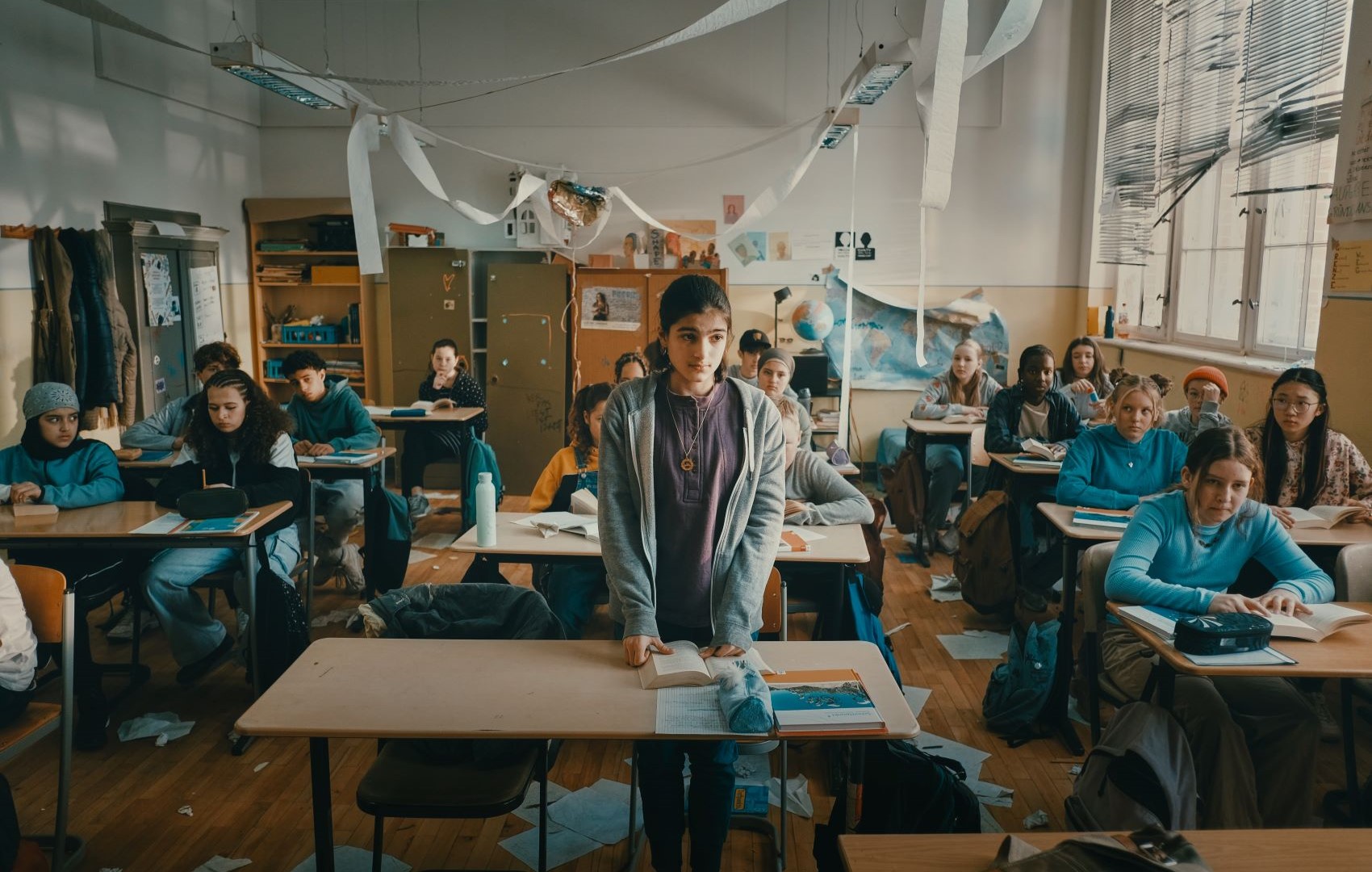 Man sieht ein Klassenzimmer mit Schülern. In der ersten Reihe ist ein Mädchen ausgestanden und beantwortet eine Frage.