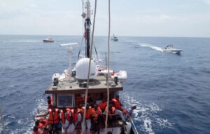 Man sieht mehrere Boote auf dem Meer. Auf dem vorderen Boot sieht man Menschen mit Schwimmwesten.